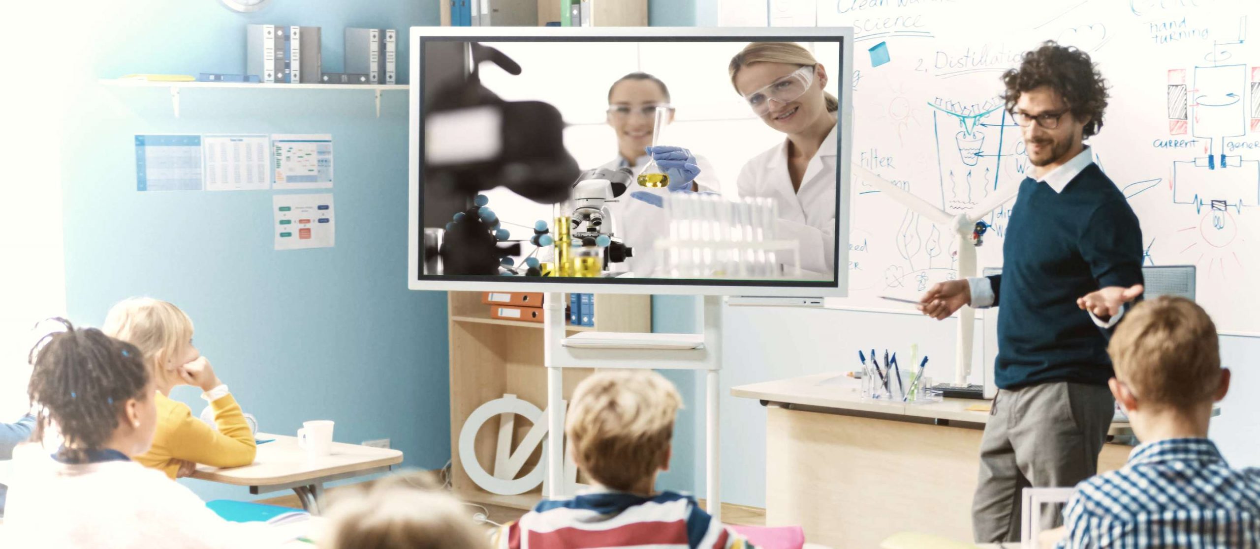 RIALE. L'immagine è presa in una classe, si vedono dei bambini che su una TV seguono in diretta l'esperimento fatto in un laboratorio remoto