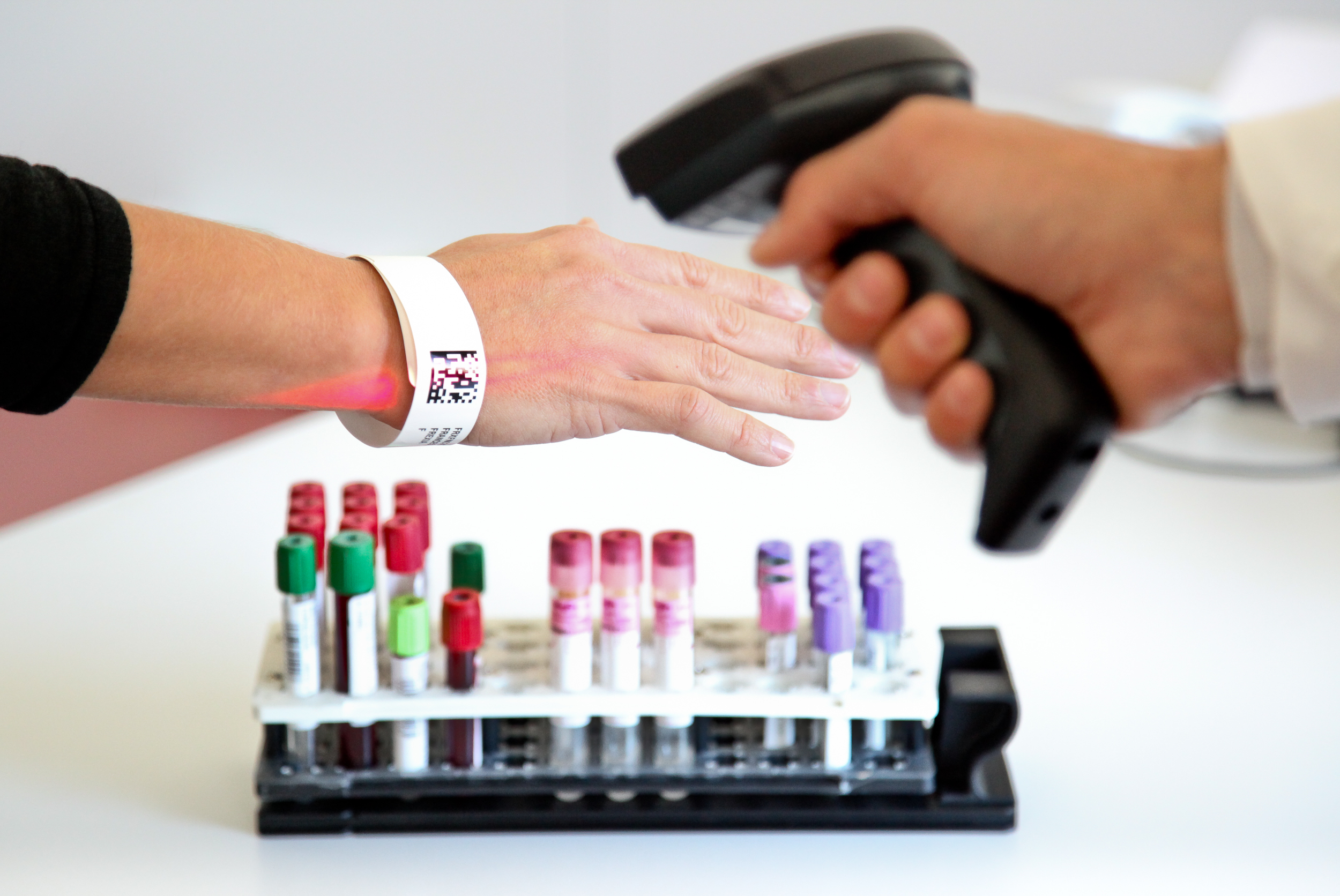 Operatore sanitario scansiona un braccialetto identificativo accanto a provette di campioni biologici in laboratorio
